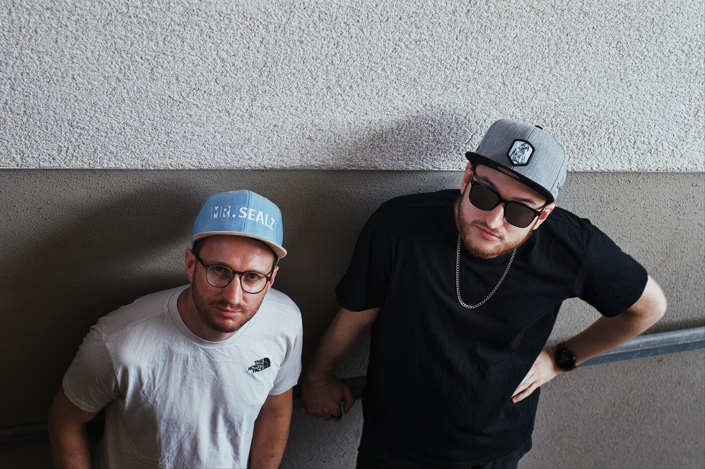 Dave und Flo in einem Säulengang, beide mit Cap und Sonnenbrille.